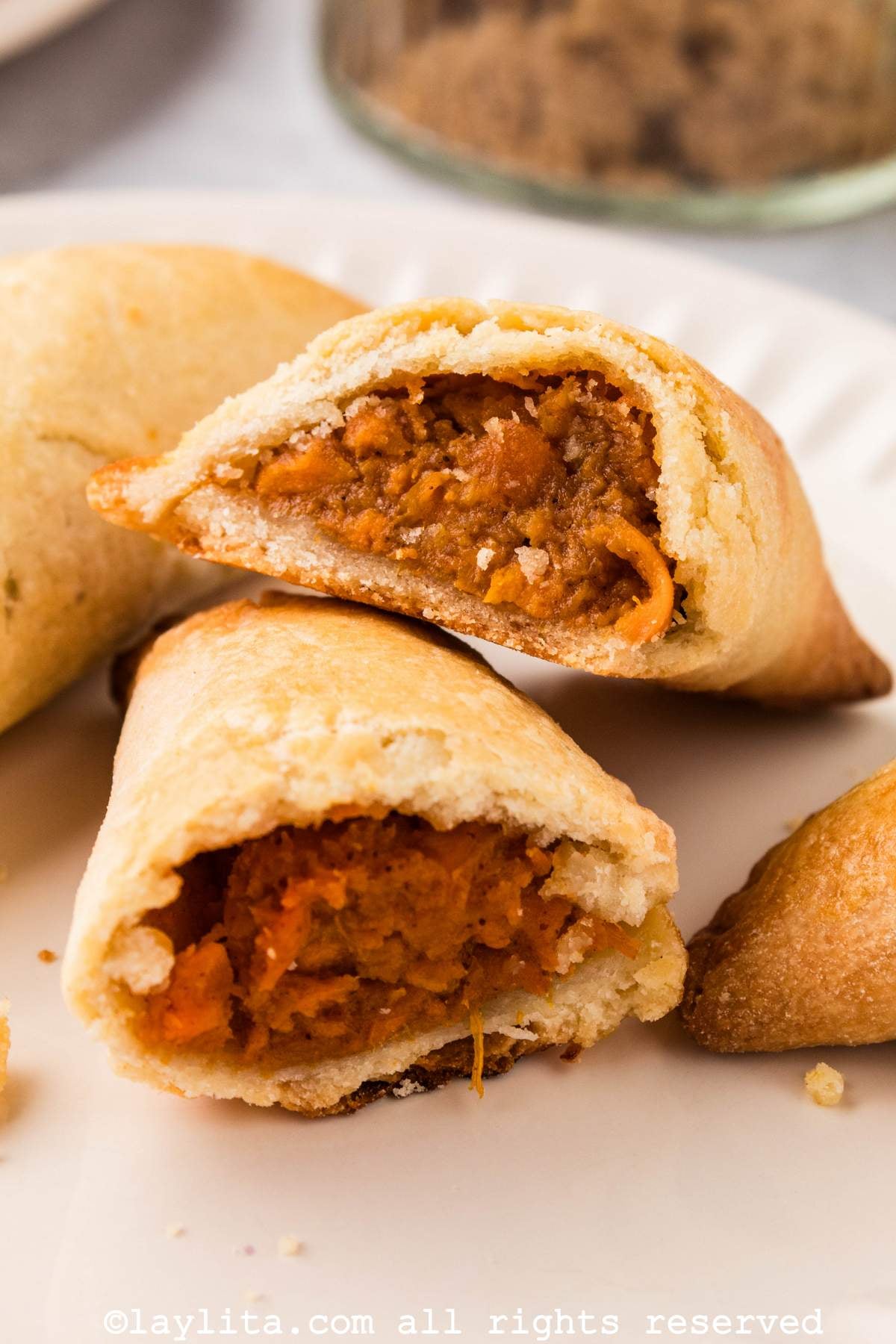 A sweet potato empanada cut in half, with the halves stacked on each other, showing the creamy filling, with more empanadas on the side