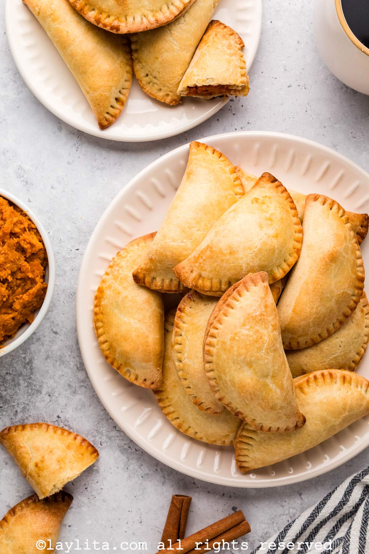 Overhead view of two white plates full of empanadas de camote, with a partial view of a bowl of creamy sweet potato on the side