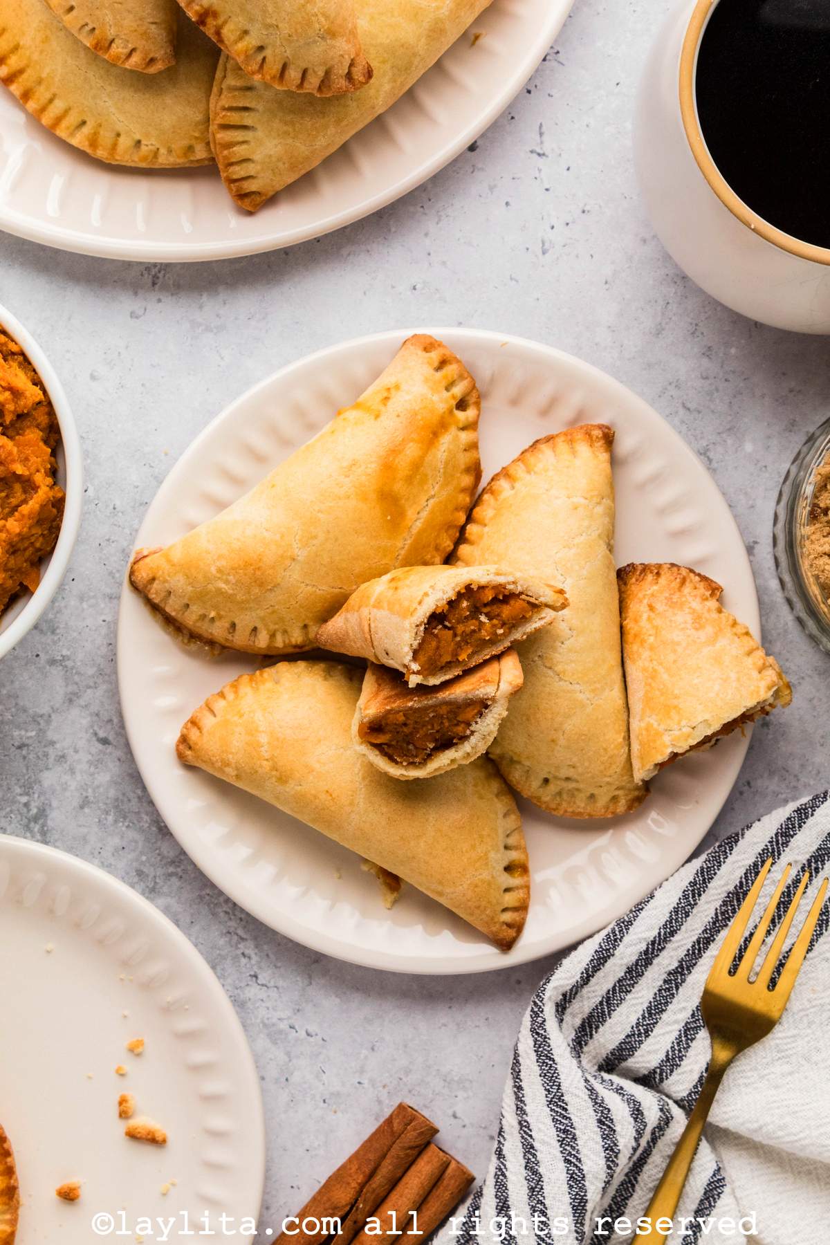 Overhead view of a plate of empanadas de camote with one cut in half showing the filling