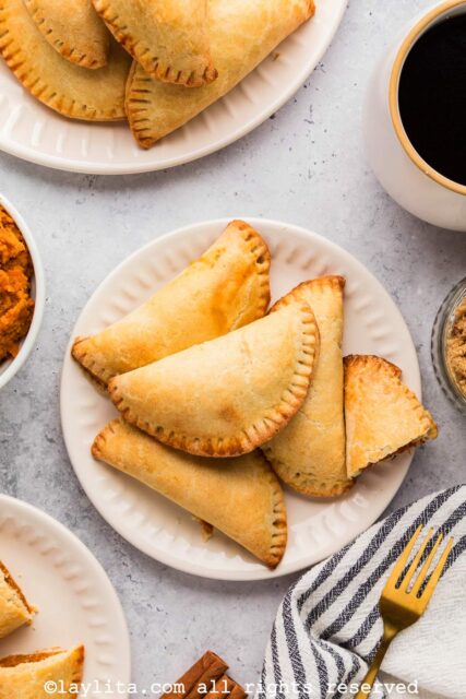 A bunch of sweet empanadas on a white plate next to a cup of coffee