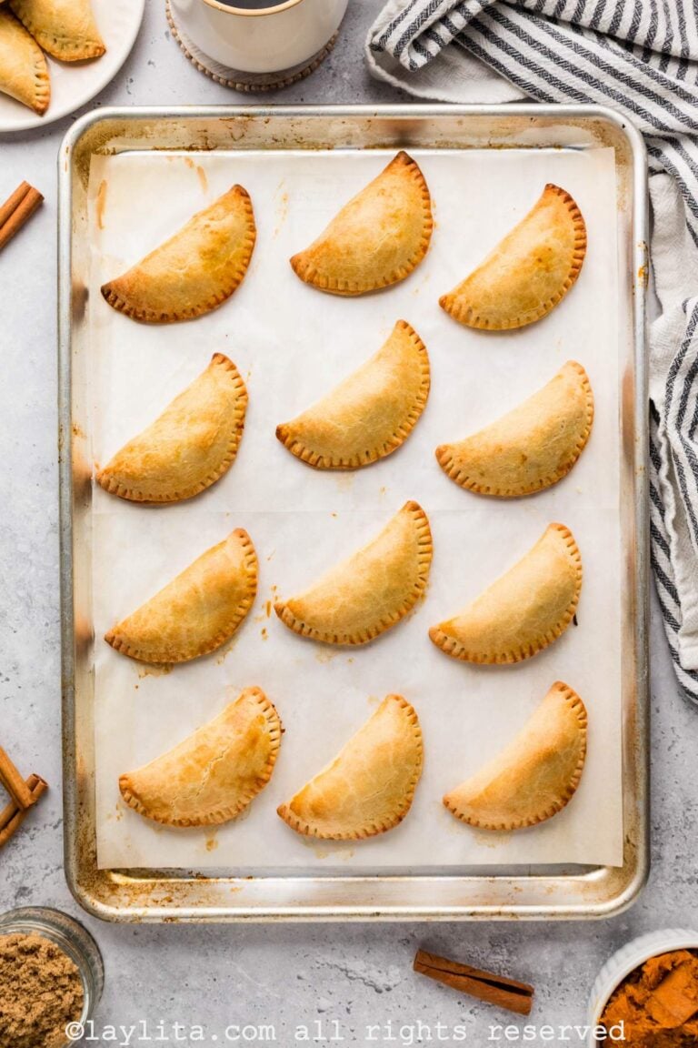 Overhead view of a tray of sweet potato empanadas, with a kitchen towel and additional empanadas on the side
