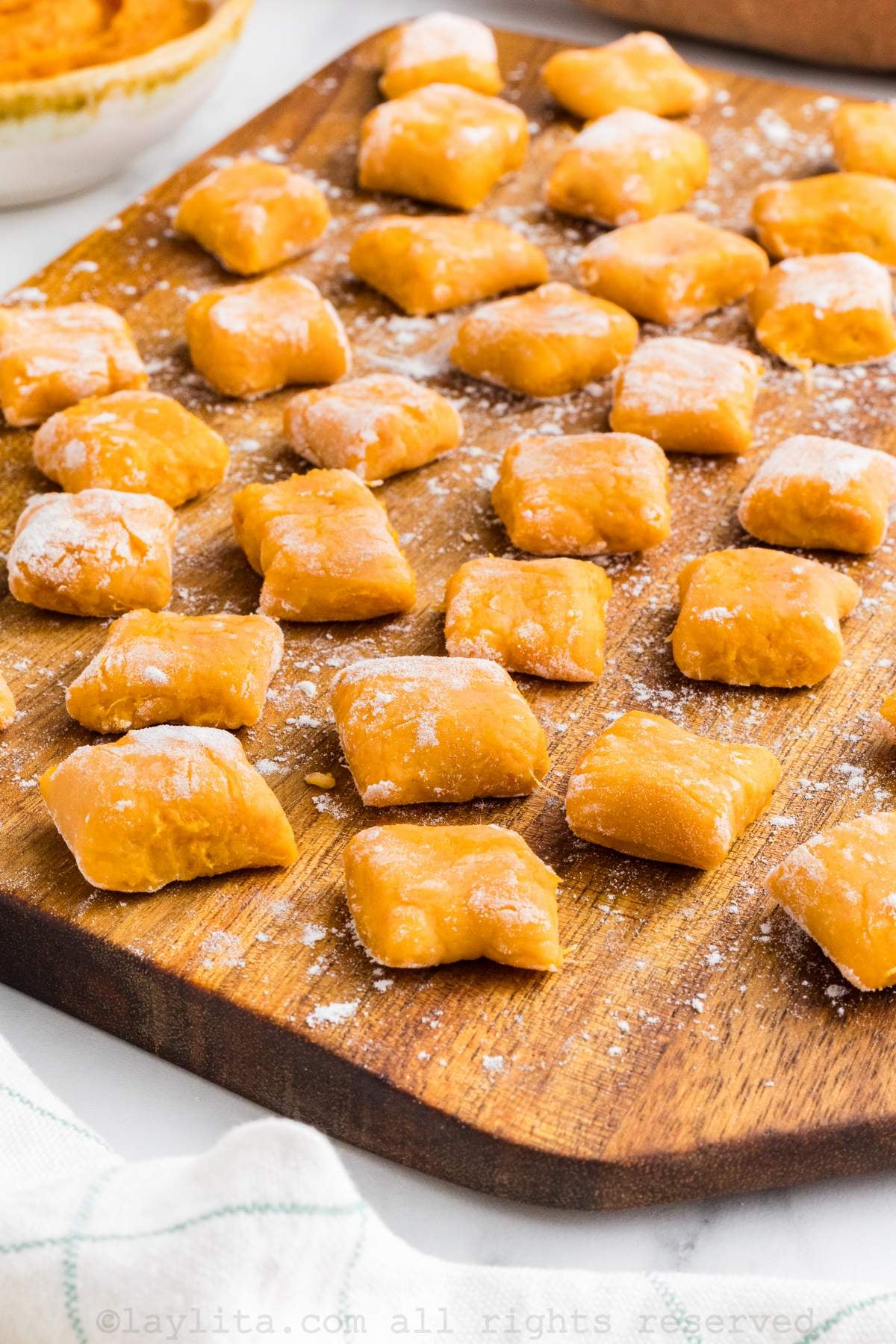 Side view of a wood board full of freshly made sweet potato gnocchis