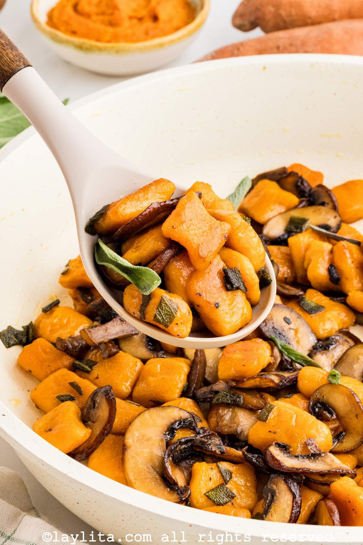 Side view of a serving spoon holding sweet potato gnocchi with mushrooms, with a skillet in the background