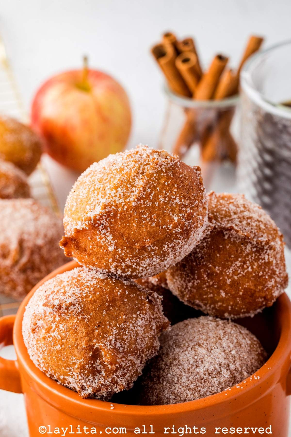 Side view of apple buñuelo fritters placed in an orange mug.
