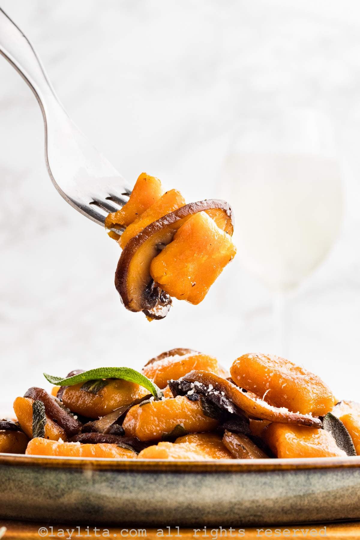 Side view of plate of sweet gnocchi and mushrooms with a fork holding a bite