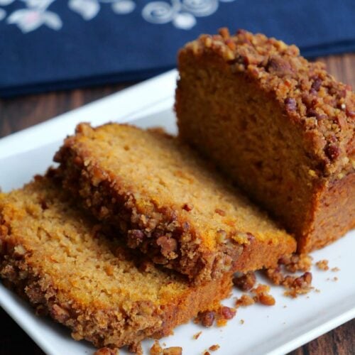 Side view of a sweet potato loaf cake topped with pecan streusel on a white plate with a couple of pieces sliced