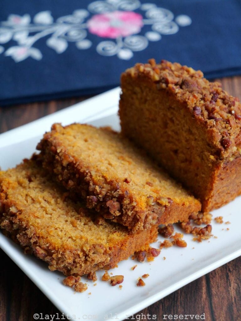 Side view of a sweet potato loaf cake topped with pecan streusel on a white plate with a couple of pieces sliced