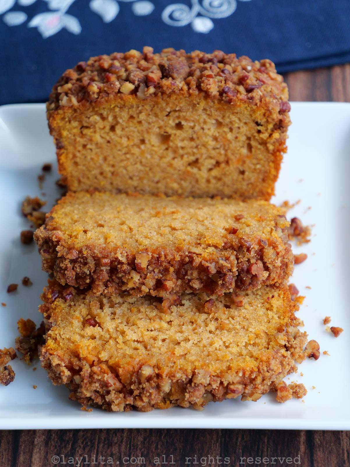 View of a sweet potato loaf cut into slices, on a white plate on top of a wood table with a blue napkin in the background