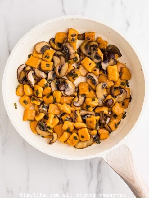 Overhead view of a white skillet full of sweet potato gnocchi sauteed with mushrooms and sage