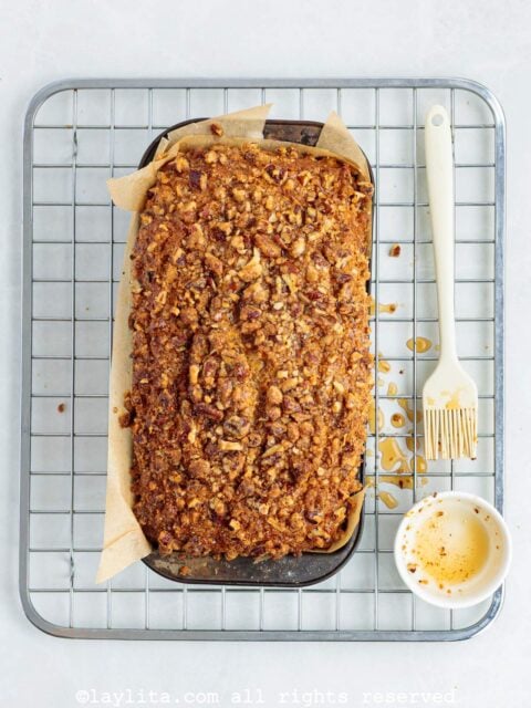 A baked sweet potato loaf on top of a cooling rack after being brushed with maple syrup