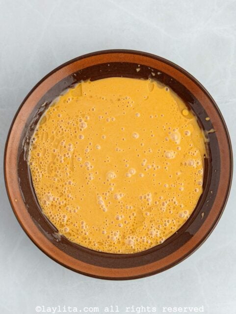 Overhead view of a mixing bowl with whisked eggs, sugar, mashed sweet potatoes and other ingredients