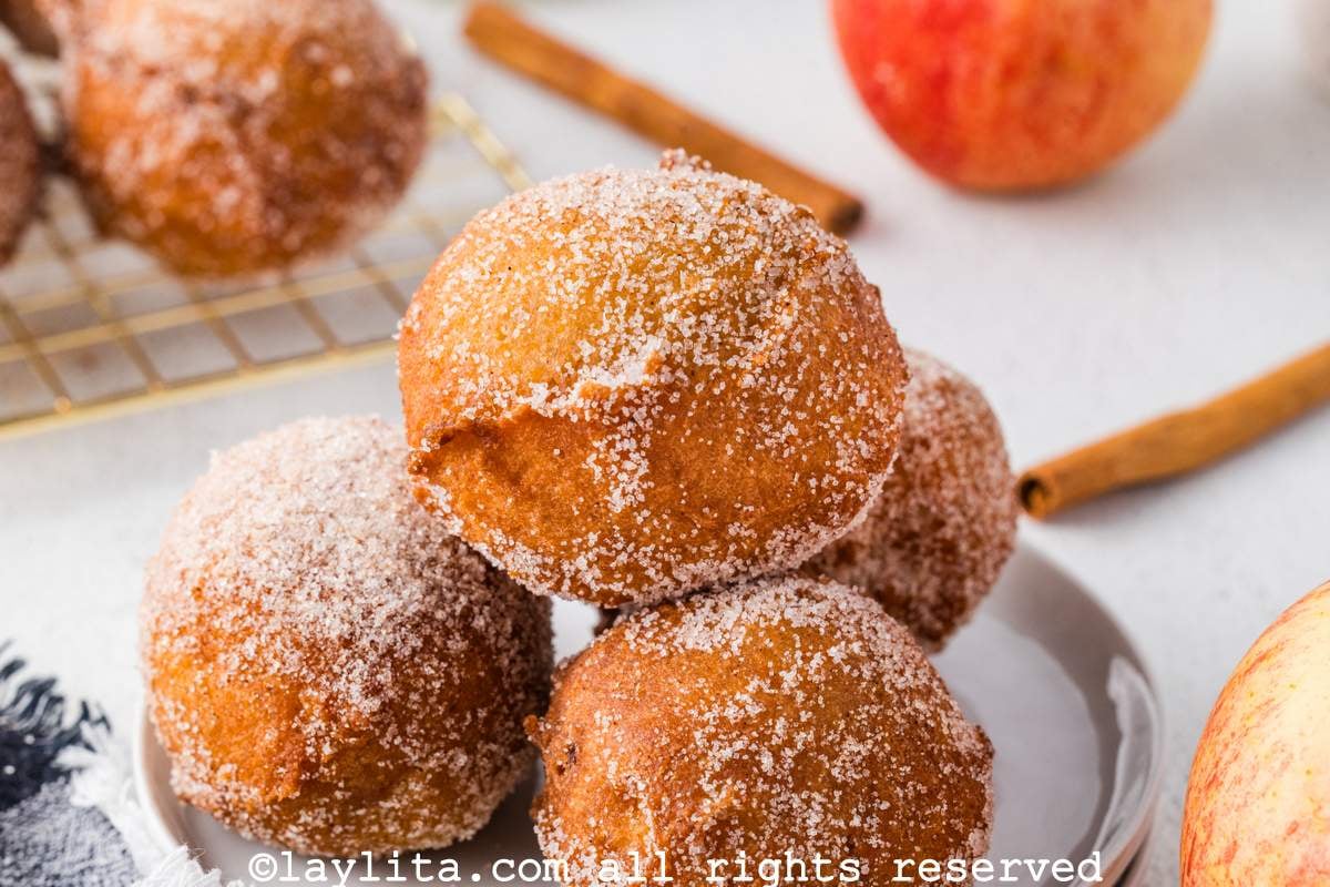 Closeup of four apple buñuelos covered in cinnamon sugar piled on a plate
