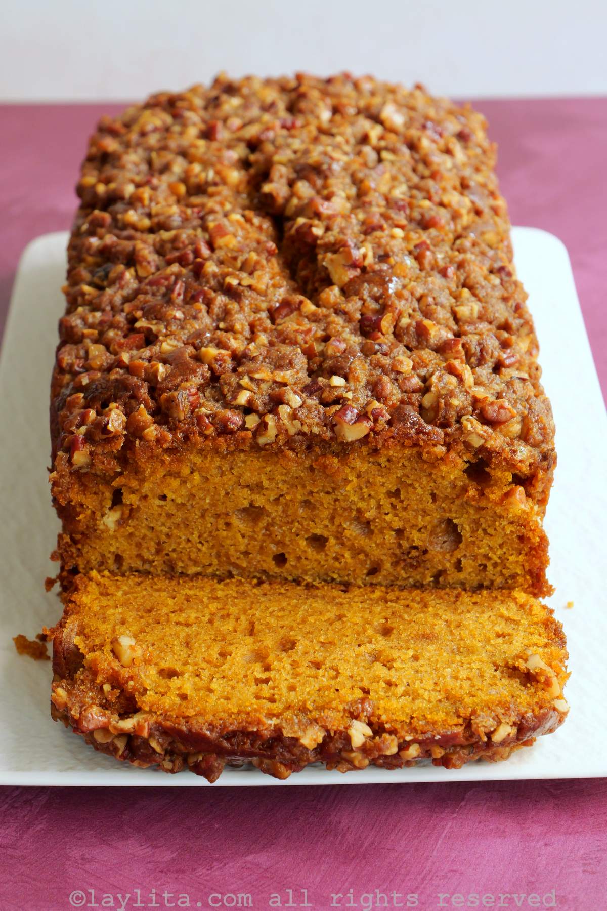A sweet potato loaf cake with pecan topping on a white plate, with a slice cut off showing the moist interior of the loaf