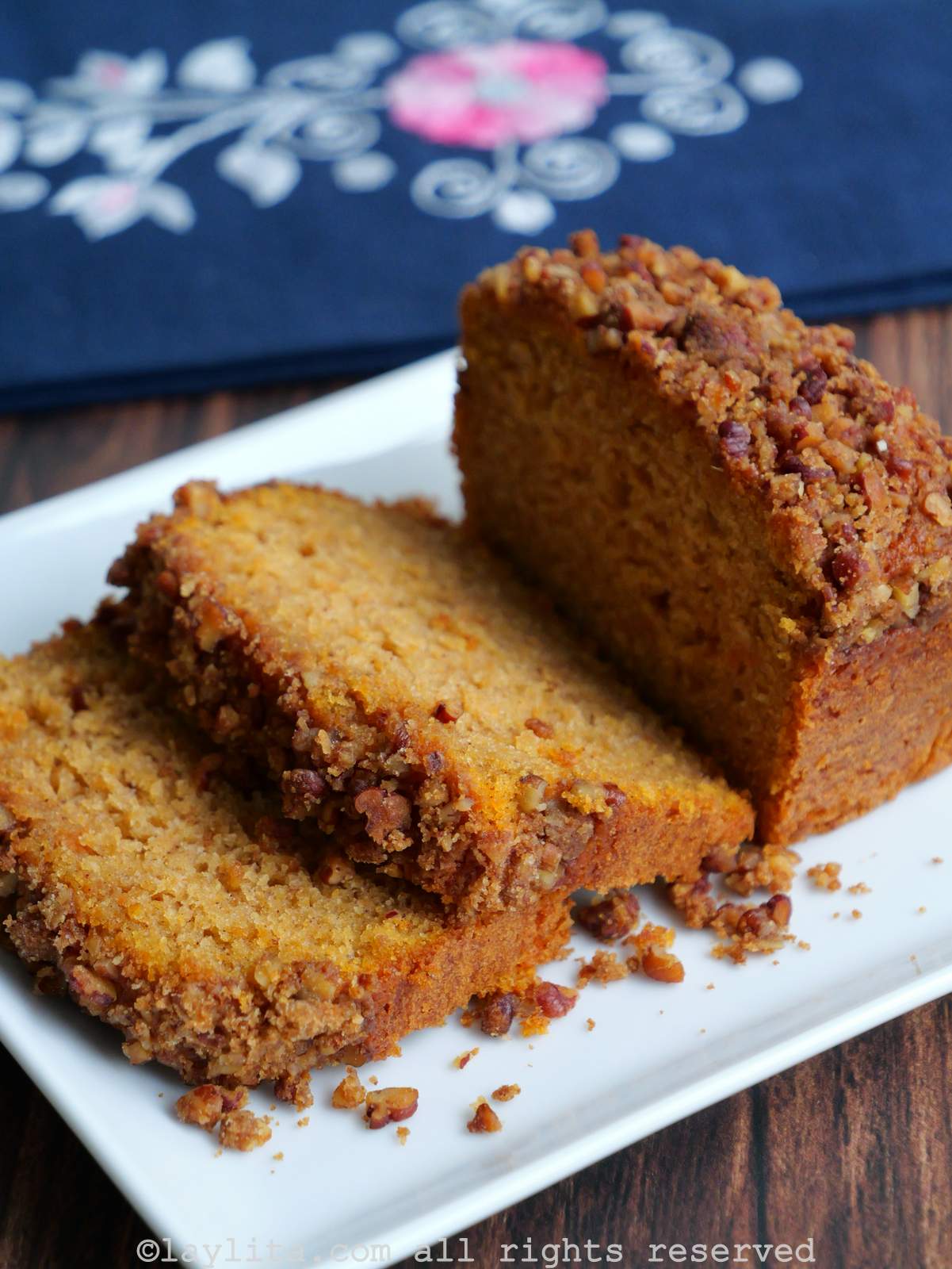 Side view of a sweet potato loaf cake topped with pecan streusel on a white plate with a couple of pieces sliced