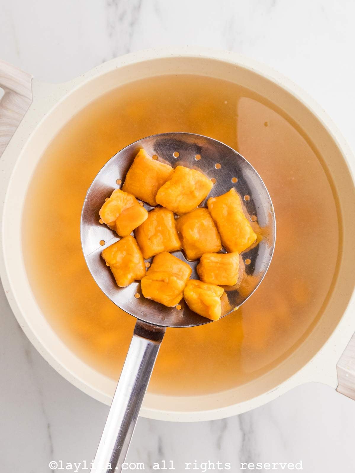 Overhead view of sweet potato gnocchi in a slotted spoon after boiling