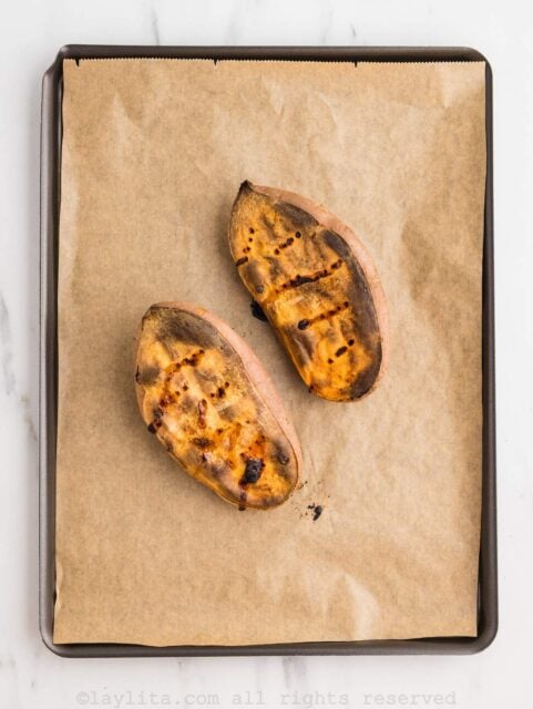 A sweet potato cut in half on a baking sheet after baking