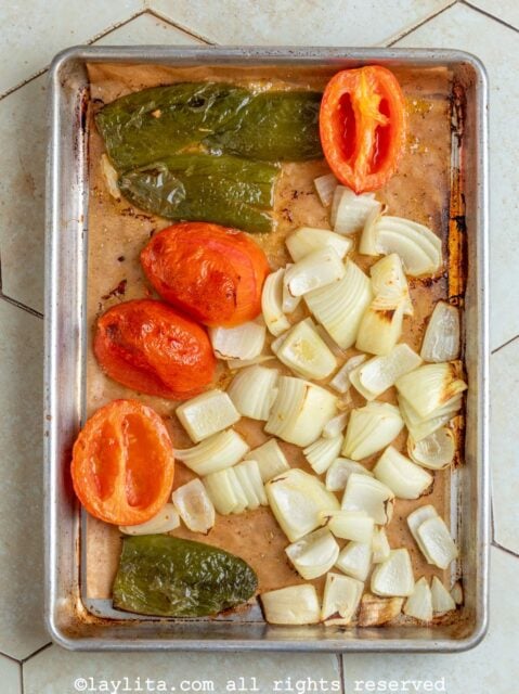 Onion chunks, tomatoes and jalapeños on a baking tray after roasting