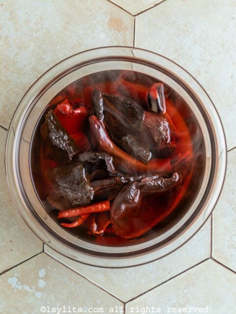 Dried red chiles rehydrating in hot water in a glass bowl