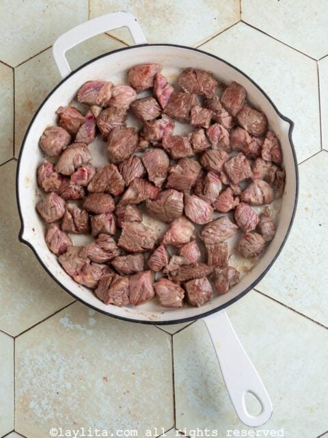 Pieces of beef being seared in a large skillet