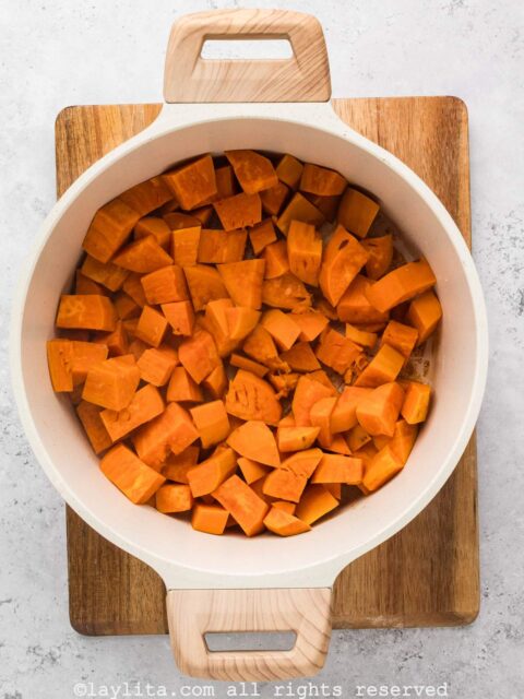 Cooking sweet potatoes with apple juice in a white pot