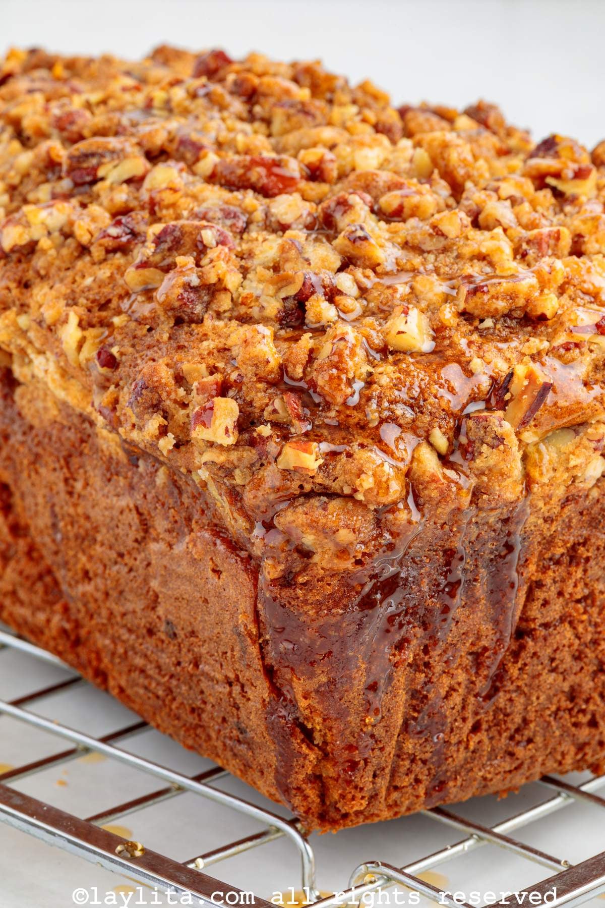 Side view of sweet potato loaf cake on cooling rack with maple syrup drizzling down the side