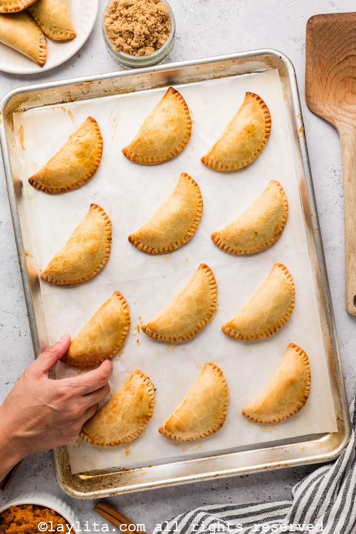 Overhead view of a tray full of sweet dessert empanadas with a hand holding one of them